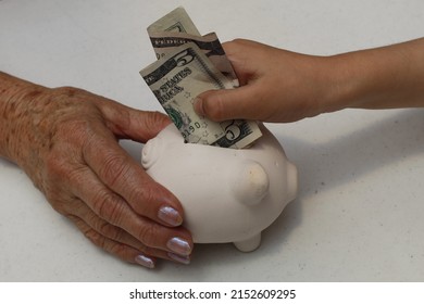 Hand Of An Older Woman Holding A Piggy Bank And Hand Of A Girl Depositing American Dollar Money