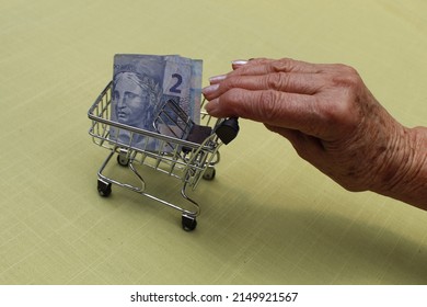 Hand Of An Older Woman Holding A Shopping Cart With Brazilian Money