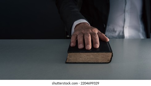 Hand on black book ,swearing on the bible , concept of telling the truth . on grey blue background .