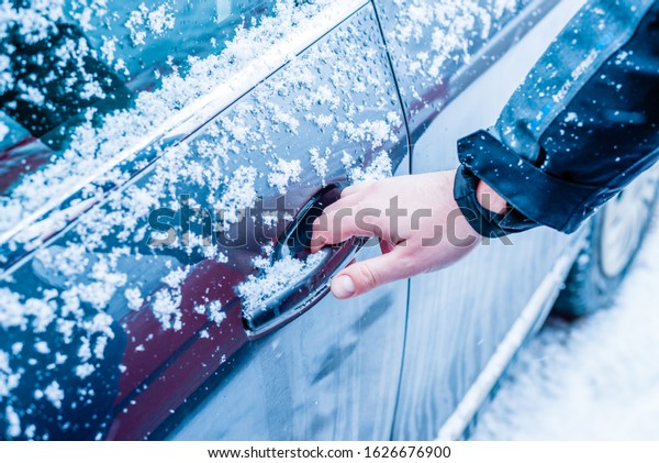 Hand on\
the door handle of a car covered in snow and ice. The concept of\
using, maintaining and cleaning the car in\
winter