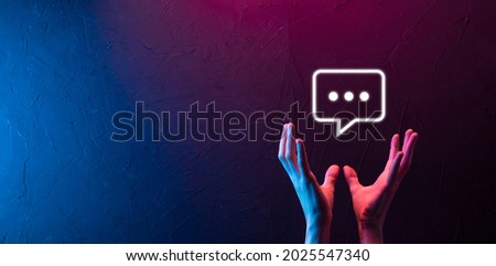 Hand on neon background holding a message icon, bubble talk notification sign in his hands. Chat icon, sms icon, comments icon, speech bubbles.