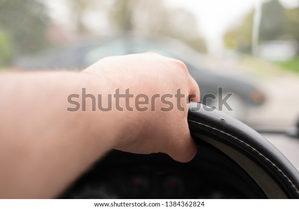 A hand on the\
steering wheel of a car.