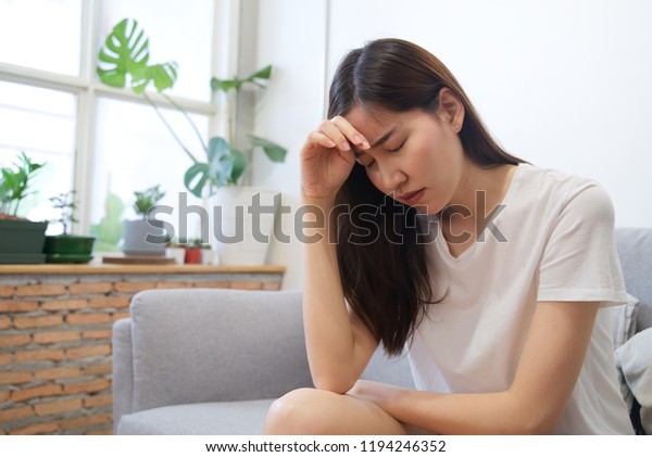 ソファに座っているアジア人の若い悲しみの情けない女の子のお寺を手渡す 彼女は病気で頭痛がしてあまり体調が良くない 正面から見た ストレスと病気のコンセプト の写真素材 今すぐ編集
