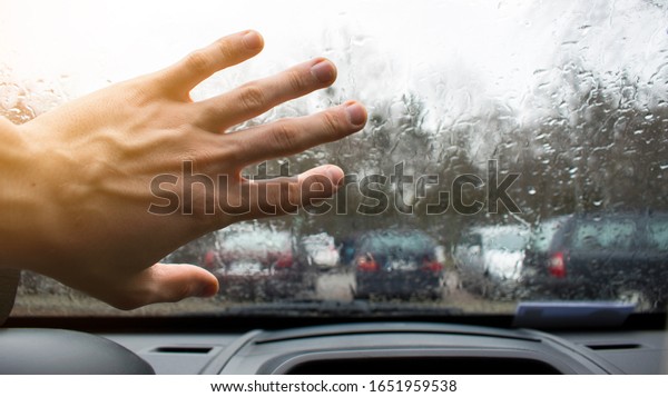 Hand on a wet car window. Raindrops outside the\
window. Rainy weather\
outside.