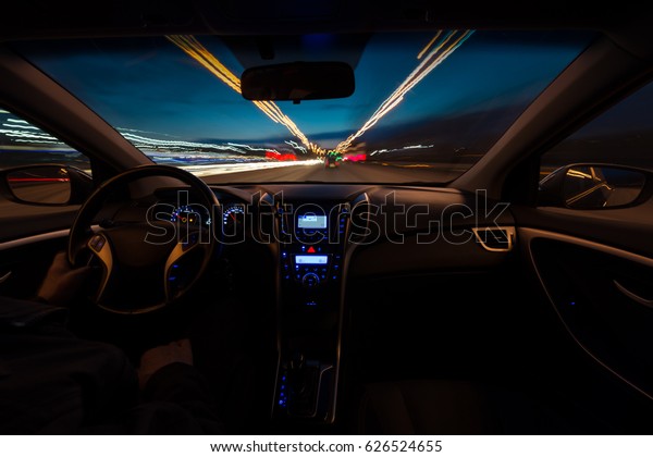 Hand on the wheel, one-handed operation. The\
car moves at a fast speed in the night of snooker. Blurred road\
with lights with a car at high\
speed