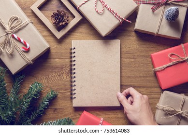 Hand Open Book With Christmas Gift Box And Tree Branch Decor On Wooden Table Background. Flat Lay, Top View With Copy Space