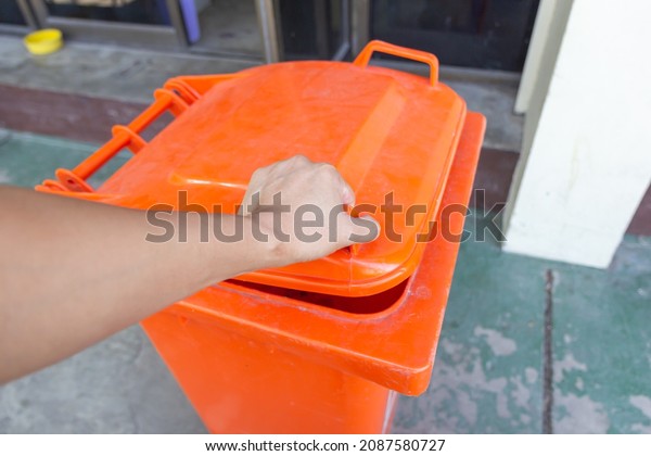 A hand opening a bin container lid before\
throwing the rubbish bag to the\
bin.