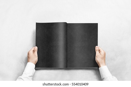 Hand opening black journal with blank pages mockup. Arm in shirt holding grey magazine template mock up. Man reading double-pages book first person view. Mag layout spread