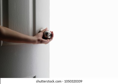 Hand opening white door knob, white background behind the door.