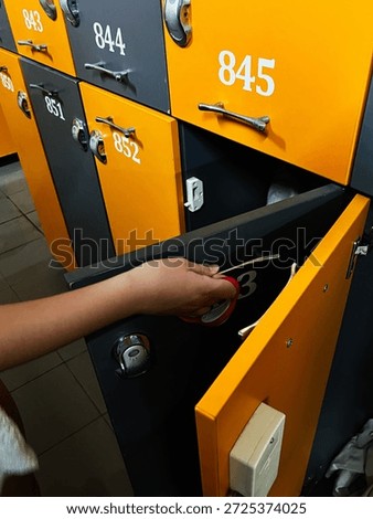 A hand opens an orange and gray locker in a row of numbered storage cabinets, showing security and organization.