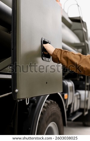 A hand opens the side compartment of a large diesel fueling truck