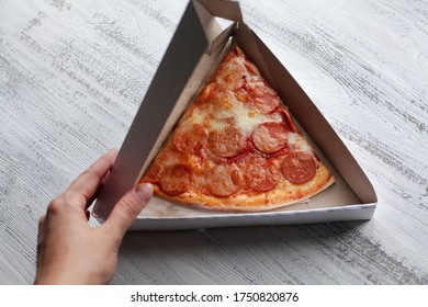 The Hand Opens A Triangular Pizza Box On A Light Background. Inside Is A Slice Of Delicious Pepperoni Pizza. Pizza Delivery At Home.