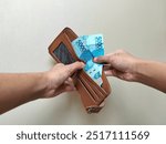 Hand opens wallet containing Rp 50,000 two notes or the same as Rp 100,000. copy space 