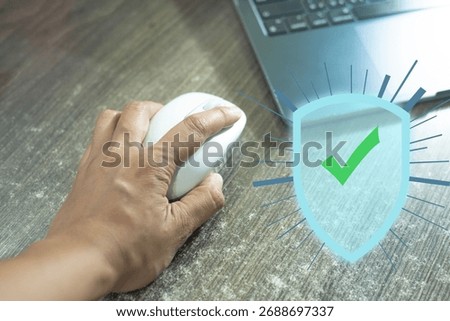 hand operates a computer mouse to a laptop, overlaid with a bright security shield and checkmark icon.Represents digital protection,cybersecurity,safe online access, antivirus software,data safety