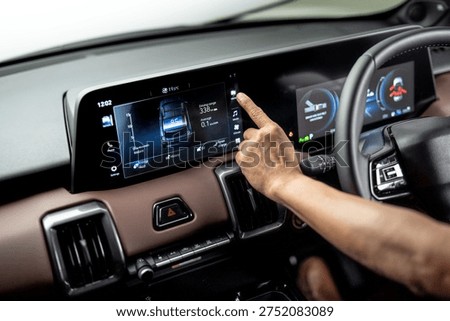 Hand operating infotainment touchscreen inside electric vehicle showing energy usage and driving range on digital dashboard display.

