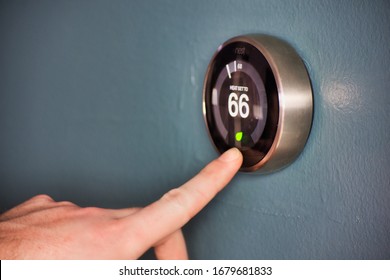 Hand Operating Smart Thermostat To Save Money