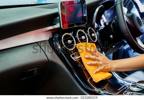 Hand\
with orange microfiber cloth cleaning interior\
car.