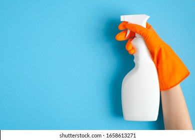 Hand in orange rubber glove holding plastic spray bottle with cleaning detergent on a blue background. - Powered by Shutterstock