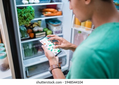 Hand Ordering Groceries Online Via Mobile Phone Apps With Open Fridge