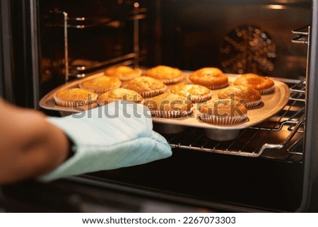 Hand, oven and muffins in baking, food or cooking sweet delicious cakes on a tray at home in the kitchen. Hands of baker taking hot muffin baked meal, treat or delight in pastry making at the house