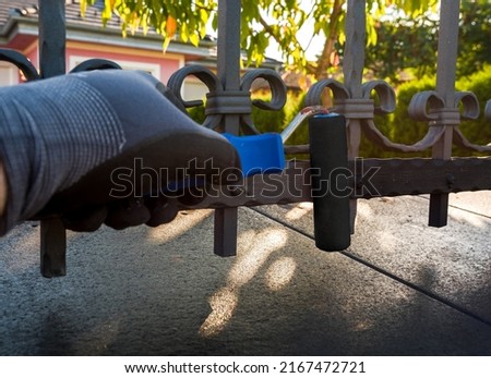 hand with paint roller painting iron fence 