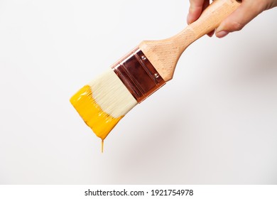 Hand With Paintbrush With Yellow Paint Drips Off The Brush