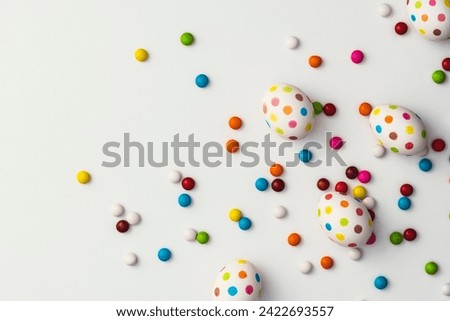 Hand painted colourful spotty easter eggs and colourful chocolate beans on white background. Directly above table top shot.