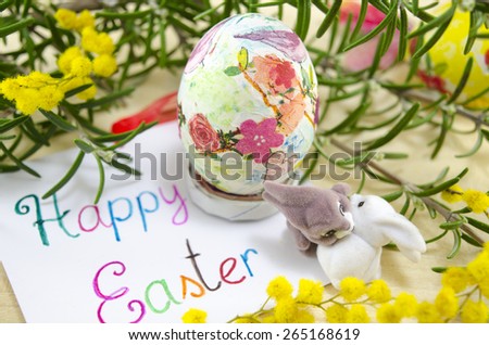 Hand painted decoupage Easter egg on woodensurface with a Happy Easter card and two toy rabbit s