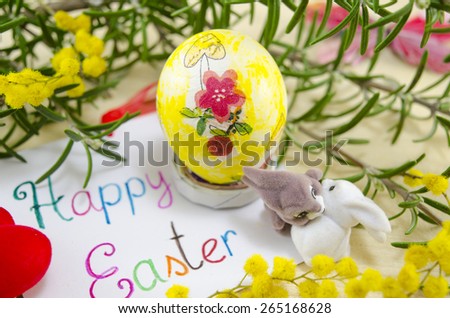 Hand painted decoupage Easter egg on woodensurface with a Happy Easter card and two toy rabbit s