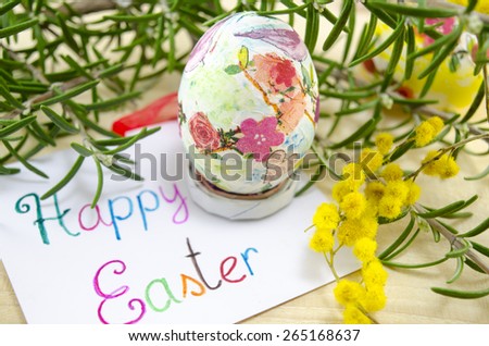 Hand painted decoupage Easter egg on woodensurface with a Happy Easter card