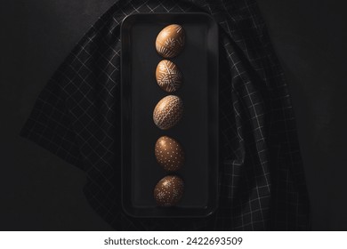 Hand painted easter eggs aligned in a row on black stoneware plate on black banckground. Directly above table top shot - Powered by Shutterstock