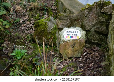 Hand painted multicoloured Beware of the Fairies sign on stone rock wall in enchanted fairy garden in woods.