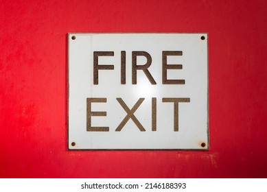 Hand painted red background with fire exit lettering on square white board scewed down at each corner