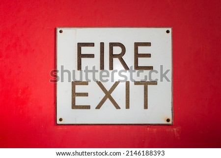 Hand painted red background with fire exit lettering on square white board scewed down at each corner