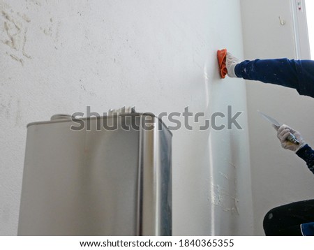 A hand of a painter holding on a piece of cloth, soaked with thinner, removing sticky rough glue and tape remain on the old concrete wall, as a preparation before starting the paint the house