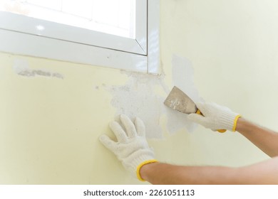 Hand painter man using scraper or spatula to remove old paint wall for cleaning, repair, preparing concrete wall before painting wall at home. Scraping to remove paint plaster peel. Painting concept.
