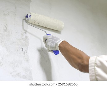 Hand painter using a roller brush to apply white paint on a wall during renovation work.
