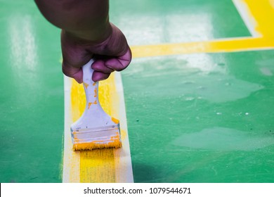 Hand Painting Yellow Action Line Marking, Safety Lines Painting In Green Floor In Industry Factory.