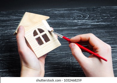 Hand Paints A House. Concept Of Repair, Hobby, Work. Repair And Painting Of Wooden House Figurines. Toy House, Work With Wood.