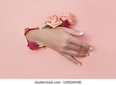 Hand With Paper Flowers And Painted Nails Is Thrust Through A Hole In The Paper Background. Cosmetics And Hand Care, Moisturizing And Wrinkle Reduction