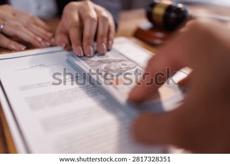Hand passing a stack of hundred dollar banknotes over a contract document, symbolizing illegal payments, bribery, judicial corruption, and the subversion of legal agreements