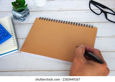 Hand with pen on blank brown notepad with space customizable for text or ideas. Copy space for ideas