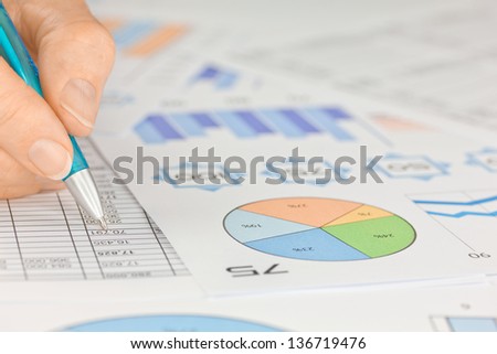 Hand with Pen working on Spreadsheet and Graphs 
