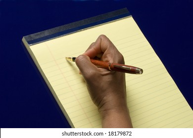Hand with pen in it writing on yellow notepad on blue background, taking notes