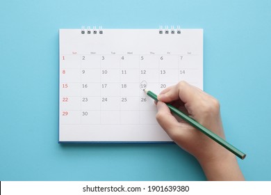 Hand With Pencil Mark On Calendar Date On Blue Background