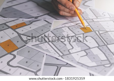 hand with pencil on cadastral map - choose and buy a building plot for house construction