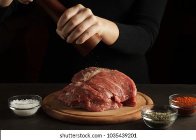 Hand Peppers Raw Meat With Pepper Mill On The Dark Background. Cooking Process Of Pork Meat.