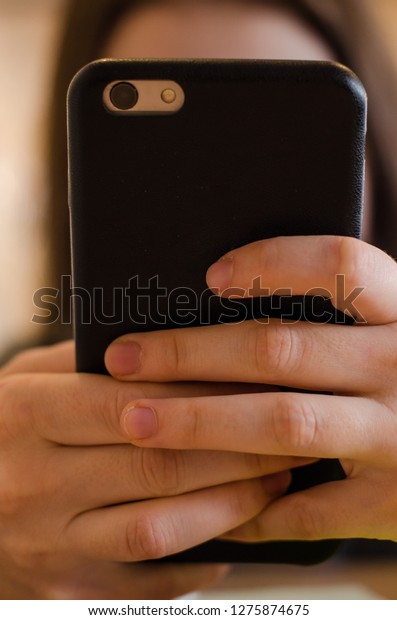 A hand of a person is holding\
the phone covering her face. A woman is using her electric\
device.