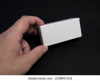 A Hand Of A Person Holding Small White Box Against The Black Background, For Mock Up