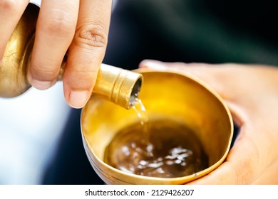 Hand person is pouring water with brass cup. Concept of making merit and dedicating charity in Buddhism.